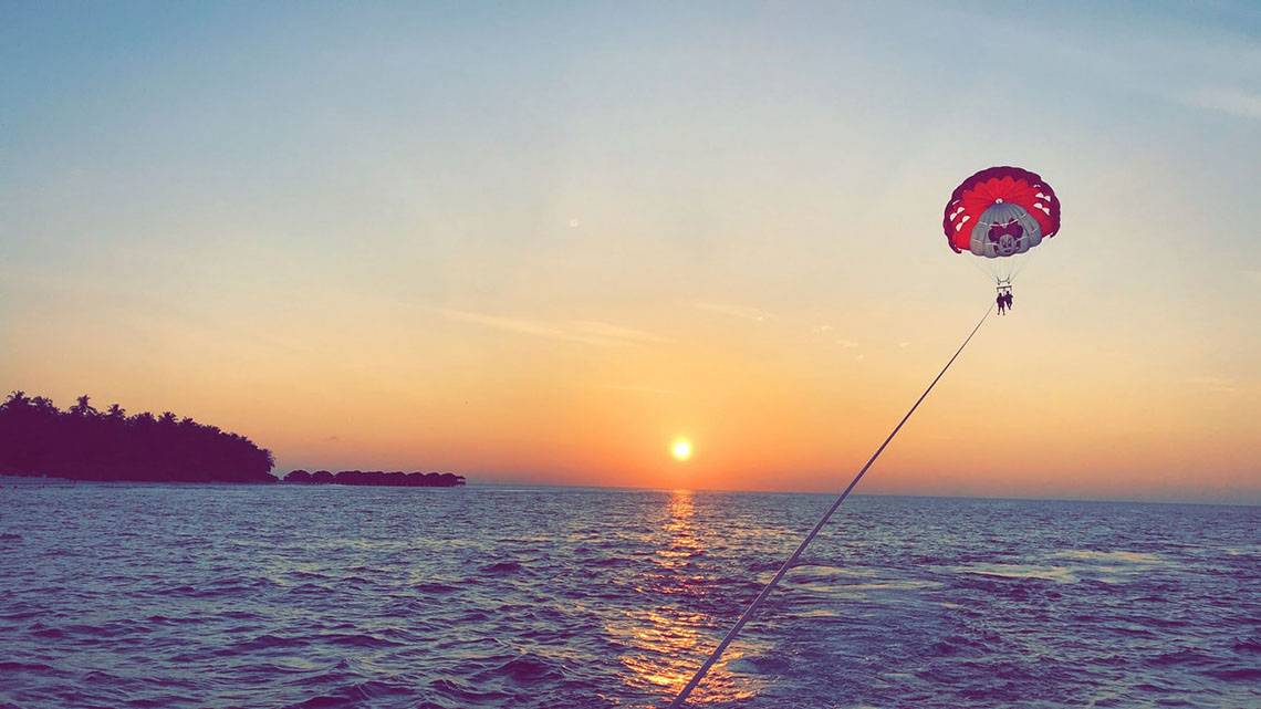 Zwei Personen parasailing bei Sonnenuntergang am Fihalhohi Island Resort.