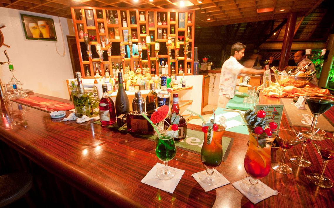 Bar im Fihalhohi Island Resort mit Cocktails, Flaschen und Barkeeper.