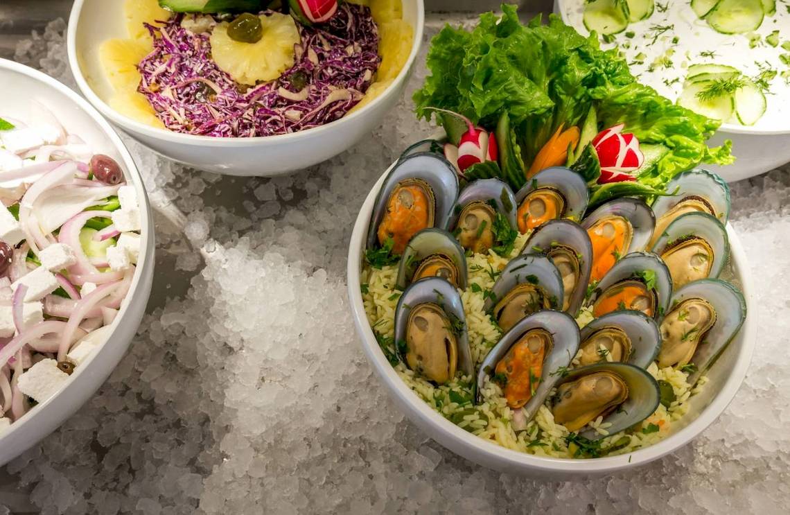 Drei Schüsseln mit verschiedenen Gerichten auf Eis, darunter eine mit Muscheln, Salat und Reis.