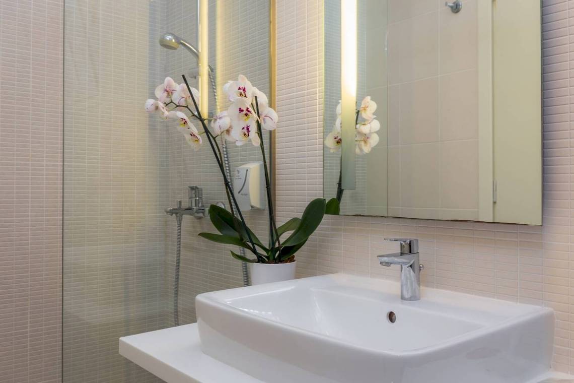 Badezimmer des Acharavi Beach Hotels mit einer weißen Badewanne, einem Waschbecken und einer Orchidee in einem weißen Topf.