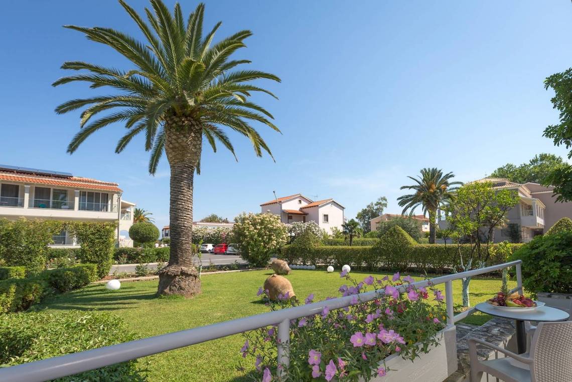 Außenansicht des Acharavi Beach Hotels mit Terrasse, Blumen und Palmen