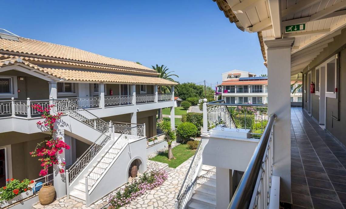Außenansicht des Acharavi Beach Hotels mit gepflegtem Garten und Balkonen.