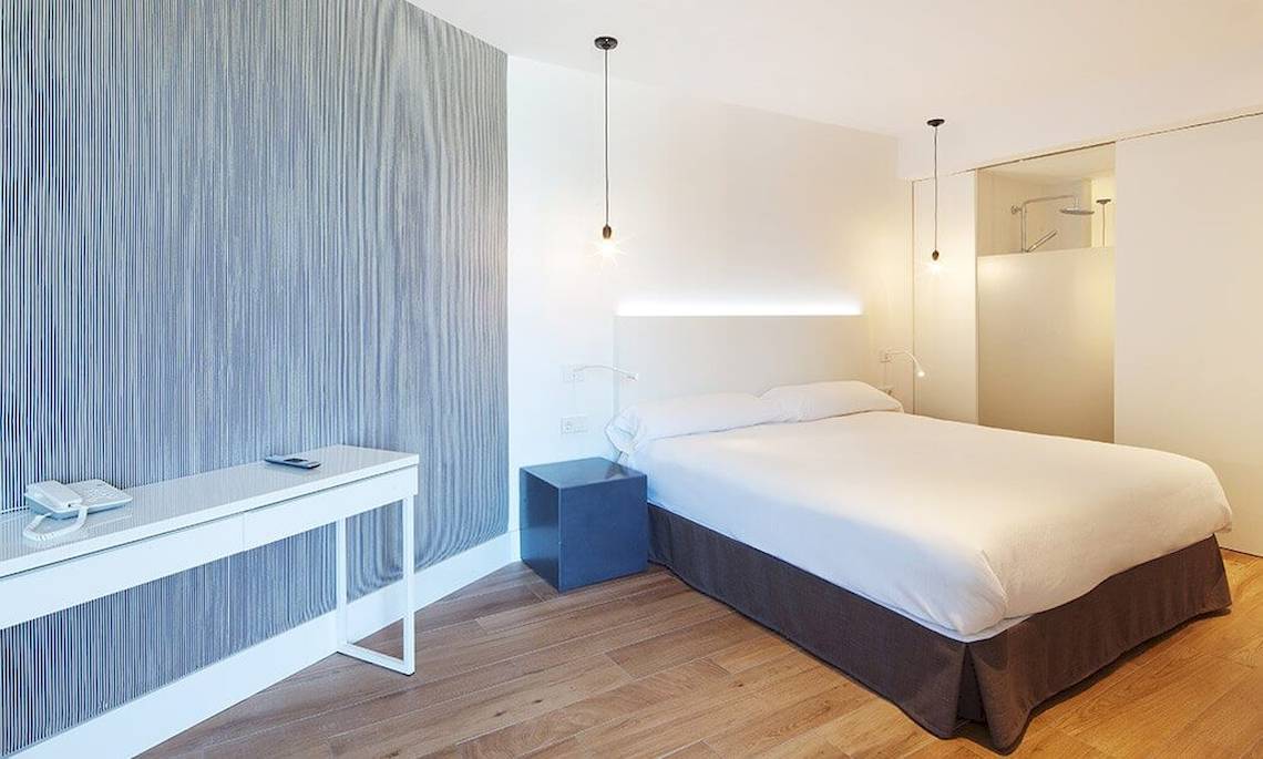 Ein elegantes Hotelzimmer im HM Gran Fiesta mit einem Bett, Nachttisch, Schreibtisch und modernen Lampen.