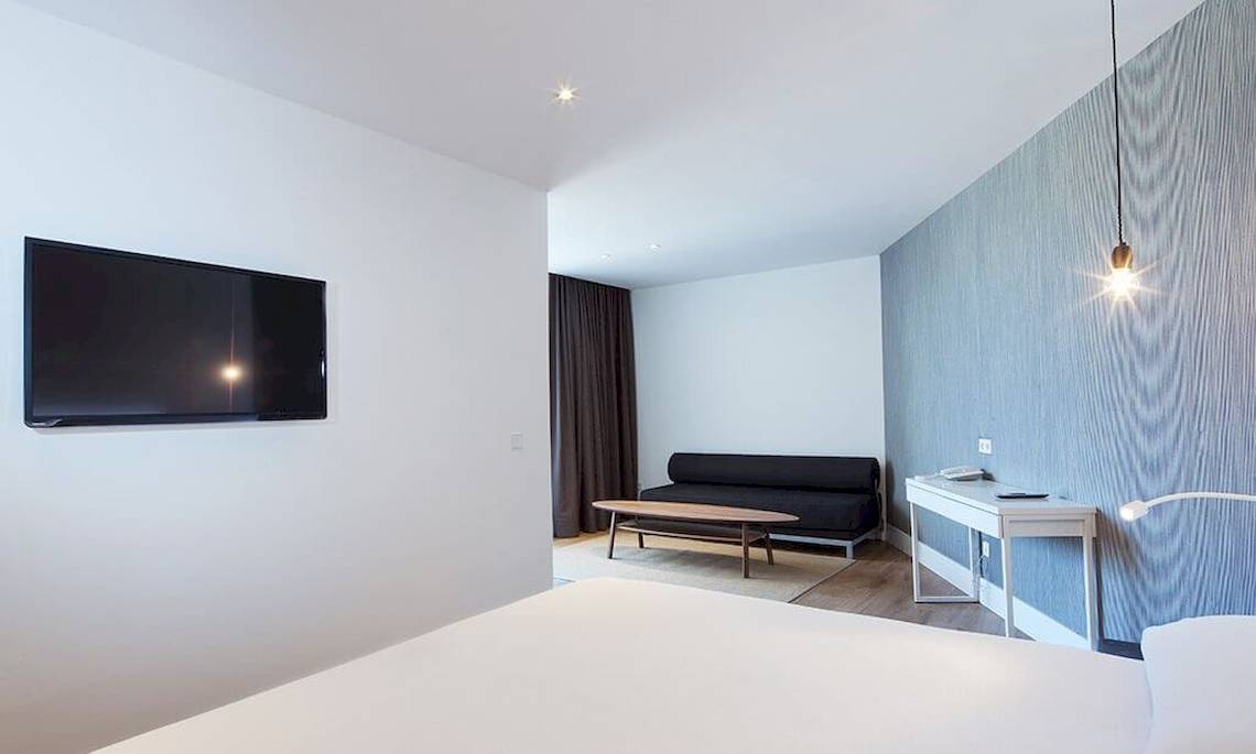Ein modernes Hotelzimmer mit Fernseher an der Wand, Sofa und Schreibtisch.