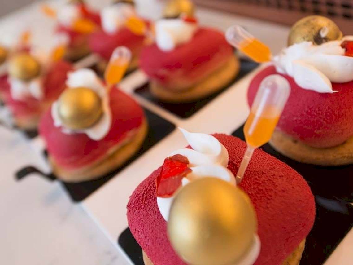 Mehrere rote Desserts mit goldenen Kugeln und orangefarbenen Stäbchen auf einem weißen Teller.