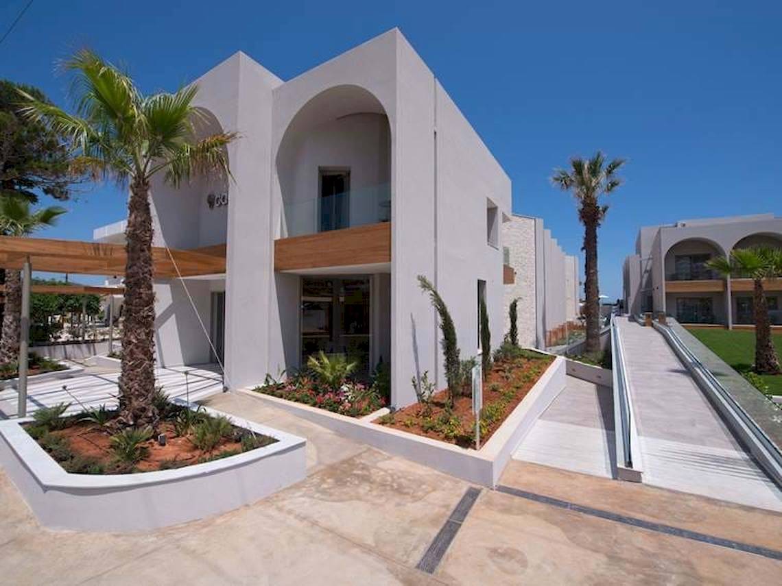 Außenansicht des Cactus Mare Hotels mit weißem Gebäude, bogenförmigen Fenstern und Palmen.