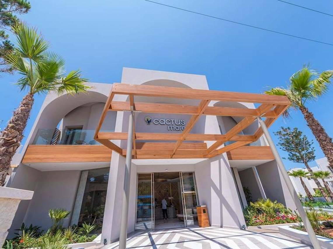 Eingang des Cactus Mare Hotels mit Holzüberdachung und Palmen im Vordergrund