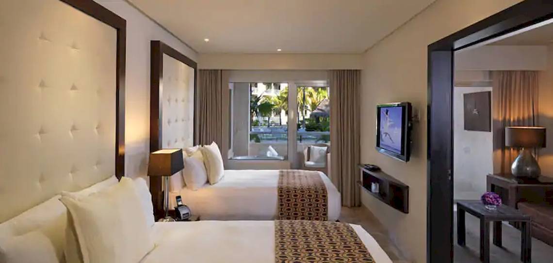 Hotelzimmer im Paradisus Playa del Carmen mit zwei Betten, Fernseher, Lampen und Aussicht auf den Außenbereich.