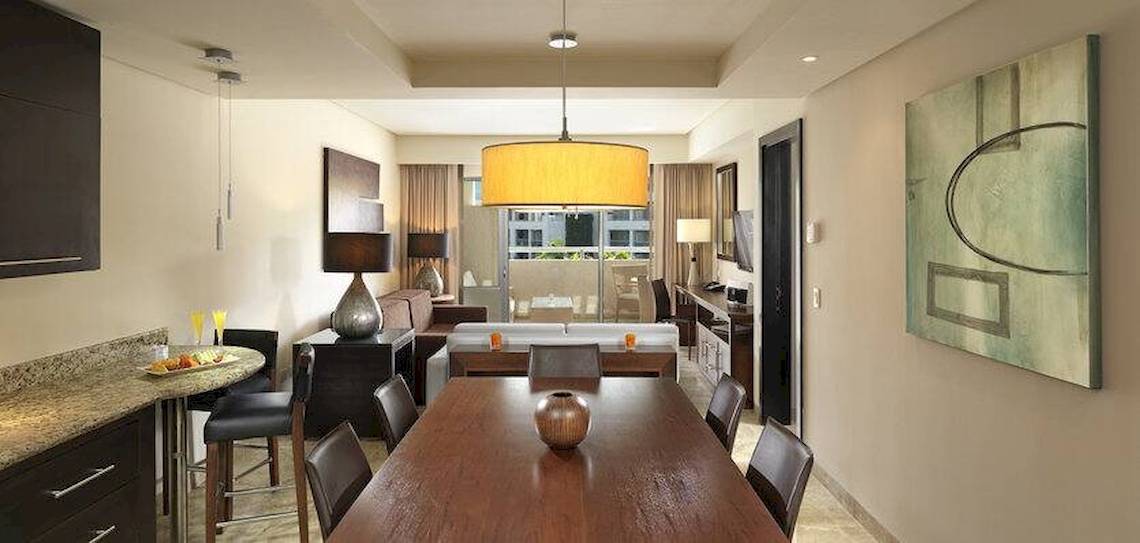 Innenansicht einer Suite im Paradisus Playa del Carmen mit Esstisch, Sofa und moderner Dekoration.