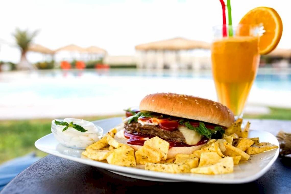 Ein Burger mit Pommes und einem Glas Orangensaft am Pool im Plaza Beach Hotel.