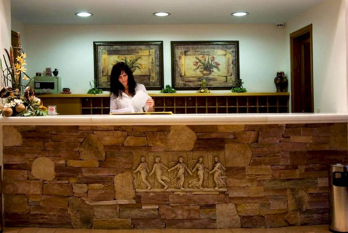 Rezeption des Plaza Beach Hotels mit einer Frau am Schreibtisch und Steinwand im Hintergrund.