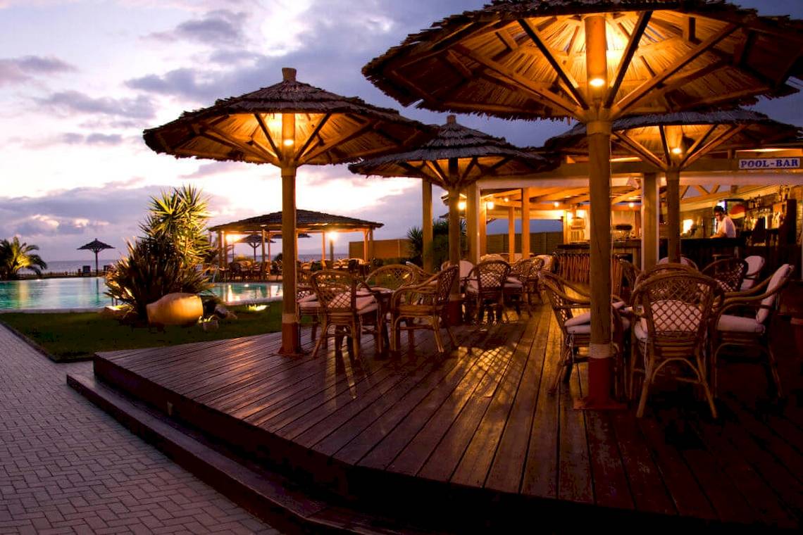 Poolbar des Plaza Beach Hotels bei Sonnenuntergang mit beleuchteten Strohschirmen und Stühlen.