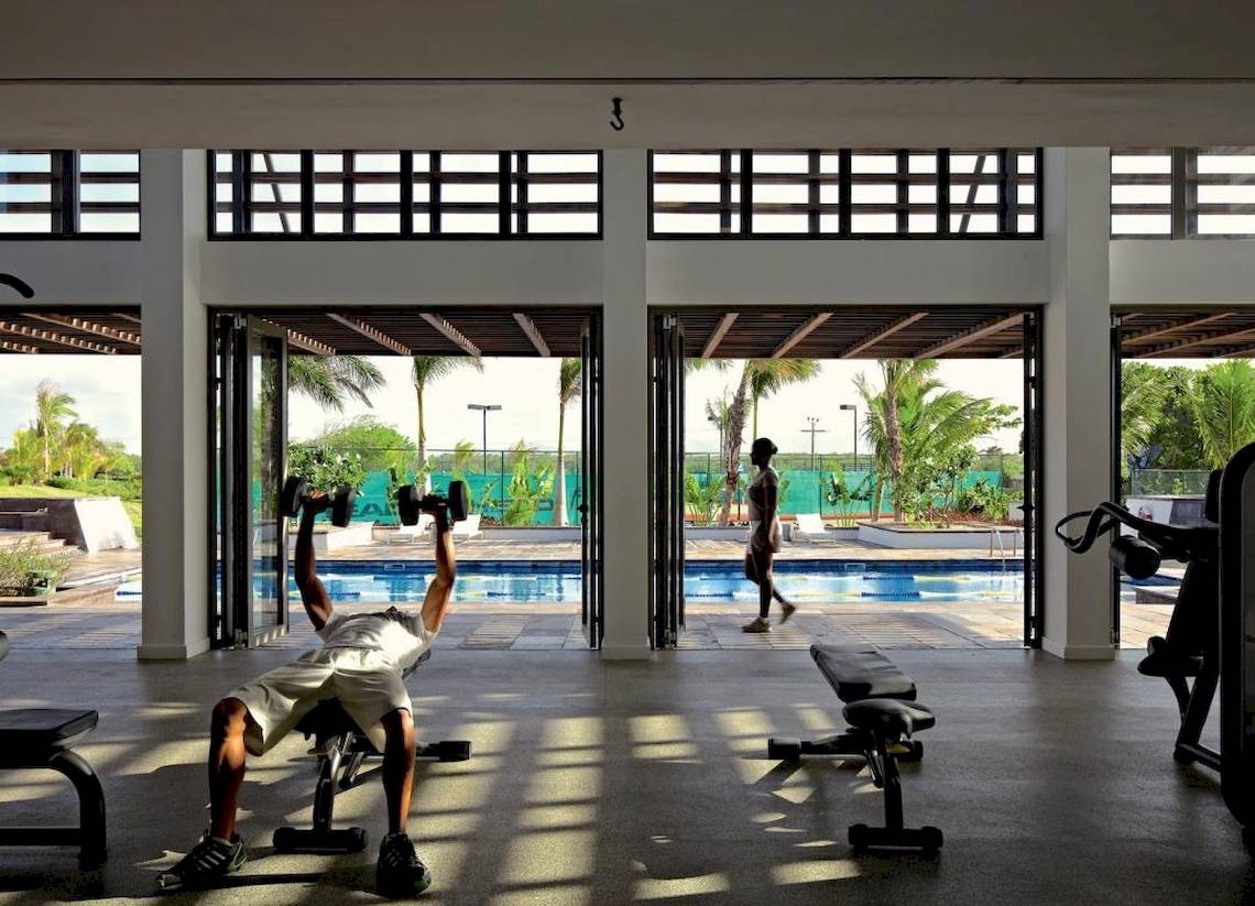 Fitnessstudio im Long Beach Mauritius mit einem Mann, der Hanteln hebt, und einem Pool im Hintergrund.