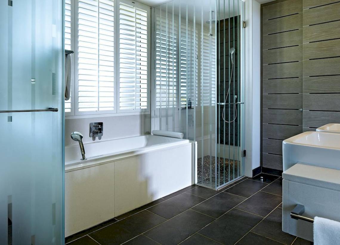 Badezimmer im Long Beach Mauritius Hotel mit Badewanne, Glasdusche und doppelwaschbecken.