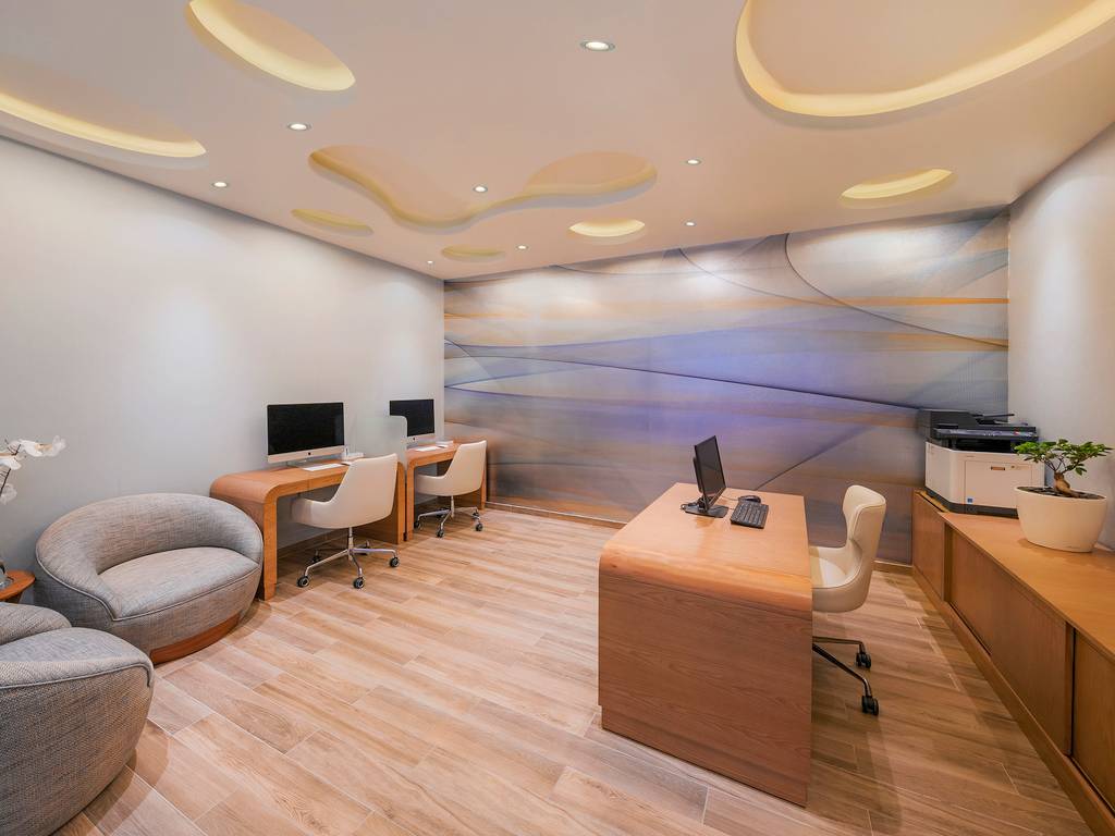 Arbeitsbereich im Hotel The Retreat Palm Dubai MGallery by Sofitel mit Computern, Sesseln und einem Schreibtisch.