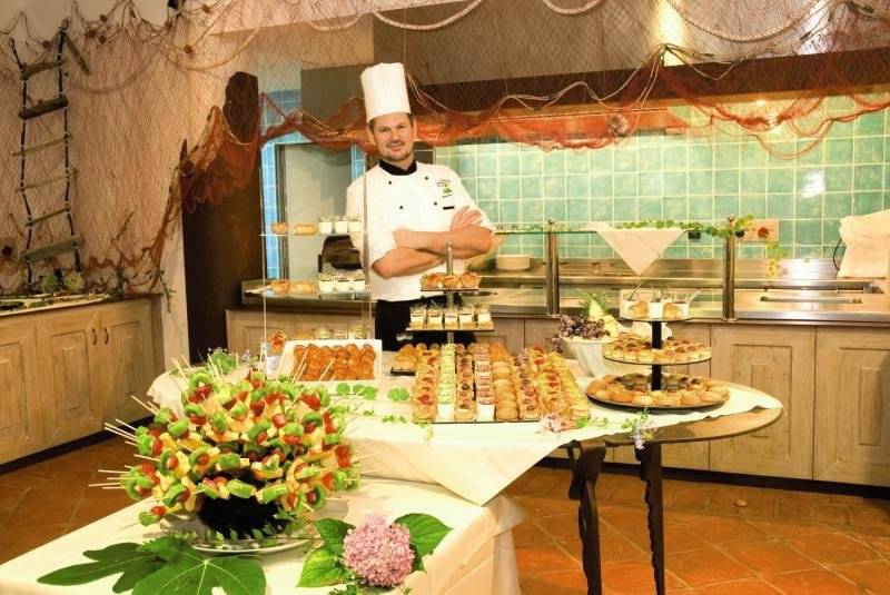 Der Küchenchef des Baia Caddinas Hotels steht vor einem Tisch voller verschiedener Desserts und Gebäck.