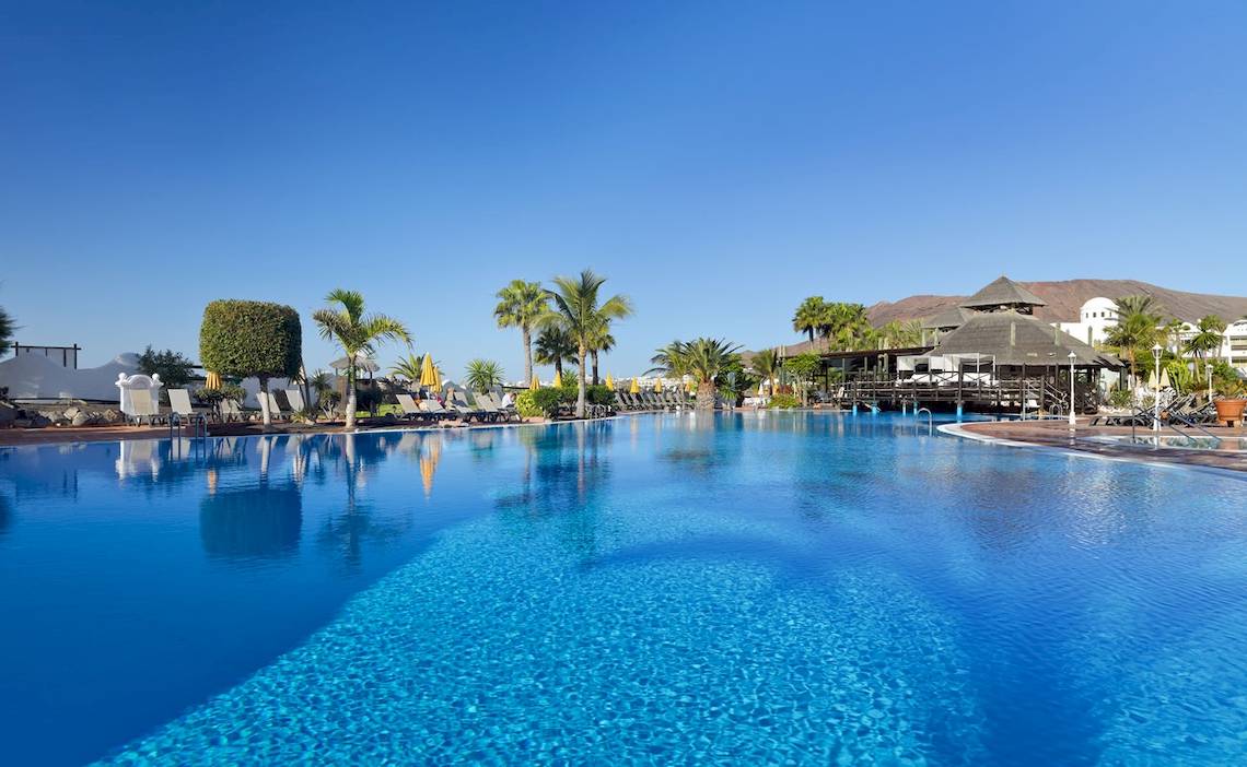 Außenpool des H10 Timanfaya Palace Hotels mit Lounge-Sesseln und Sonnenschirmen.