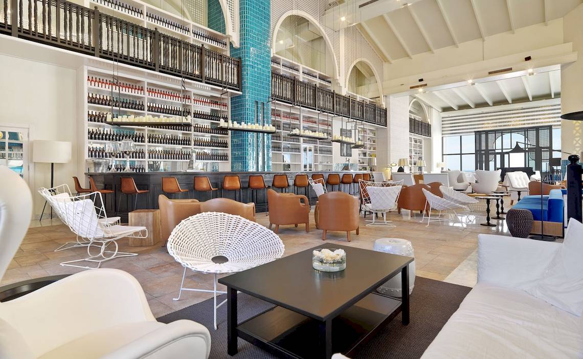 Loungebereich im H10 Timanfaya Palace Hotel mit weißen Möbeln und einer zentralen Bar.