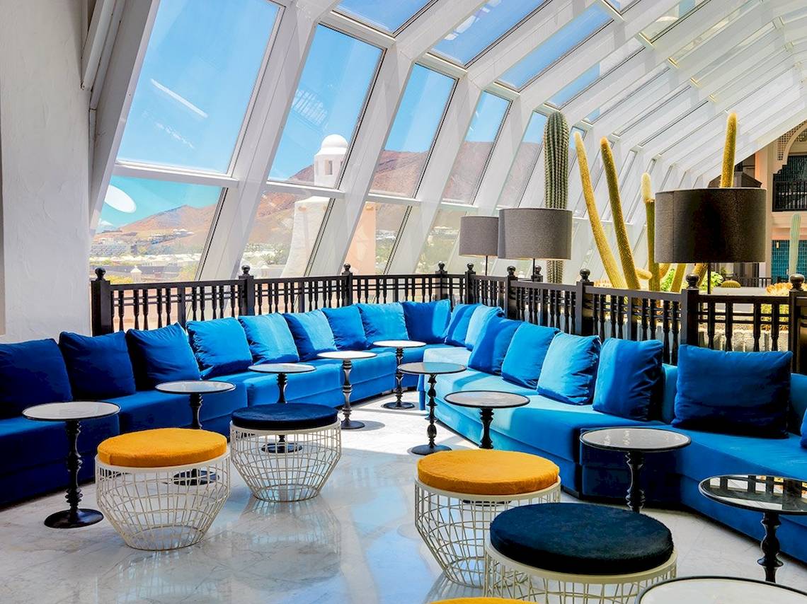 Loungebereich des H10 Timanfaya Palace Hotels mit blauen Sofas, orangen Hockern und Tischen.