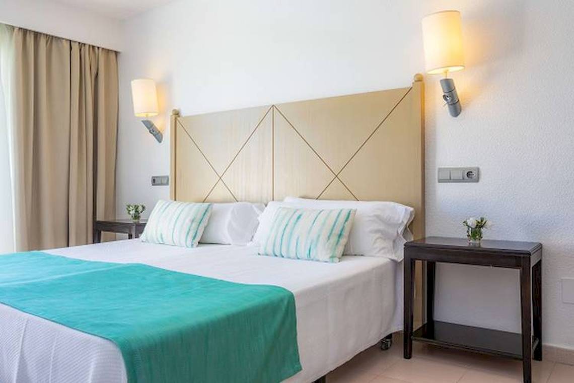 Schlafzimmer im Blau Punta Reina Hotel mit Doppelbett, Nachttischen und Wandleuchten.