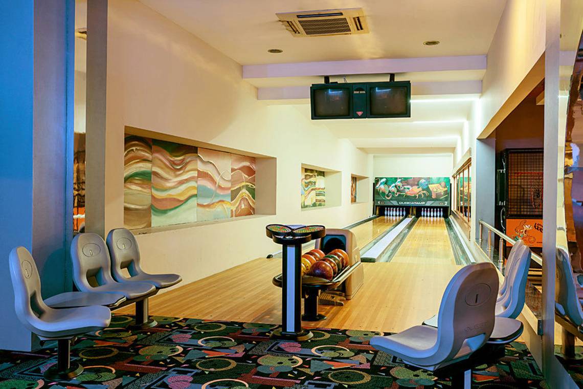 Innenraum der Bowlinghalle im Sunis Kumköy Beach Resort & Spa mit Bowlingbahnen, Sitzbänken und Gemälden an der Wand.