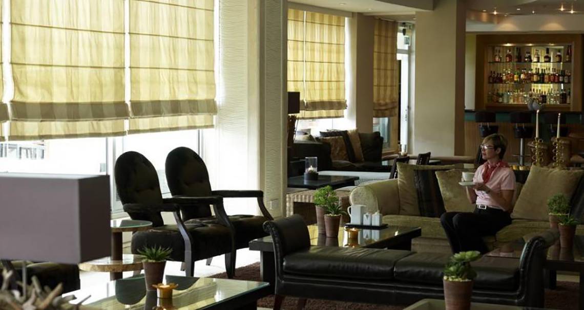 Frau sitzt in der Lobby des Atlantica Miramare Beach Hotel mit Kaffeetasse