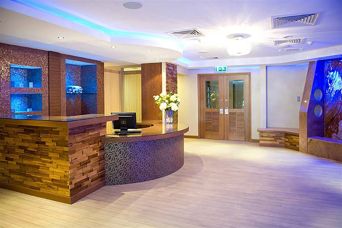 Rezeption des Atlantica Miramare Beach Hotels mit Holzwand, Blumenvase und blau beleuchteten Nischen.