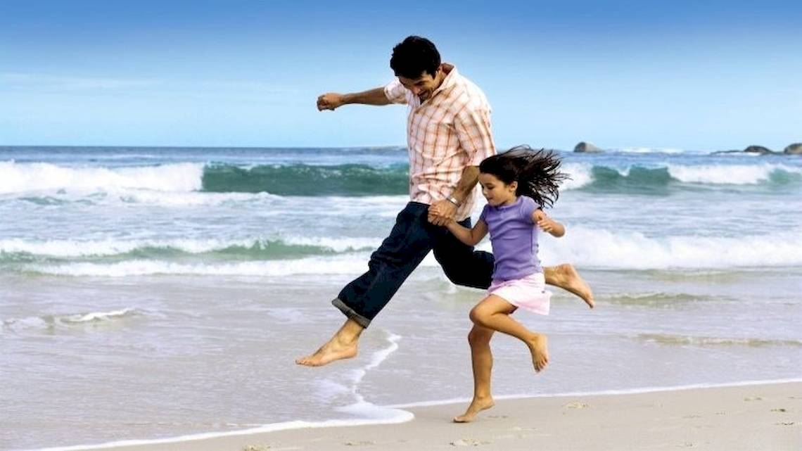 Ein Vater und seine Tochter springen am Strand von Brayka Bay Resort.