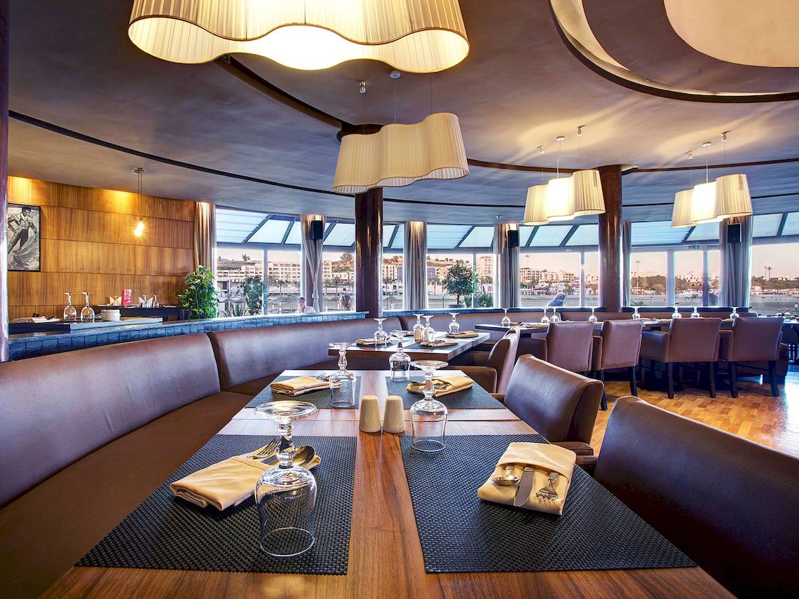 Innenansicht des Restaurants im Bianca Beach Resort mit Tisch, Gläsern und Blick auf die Stadt.