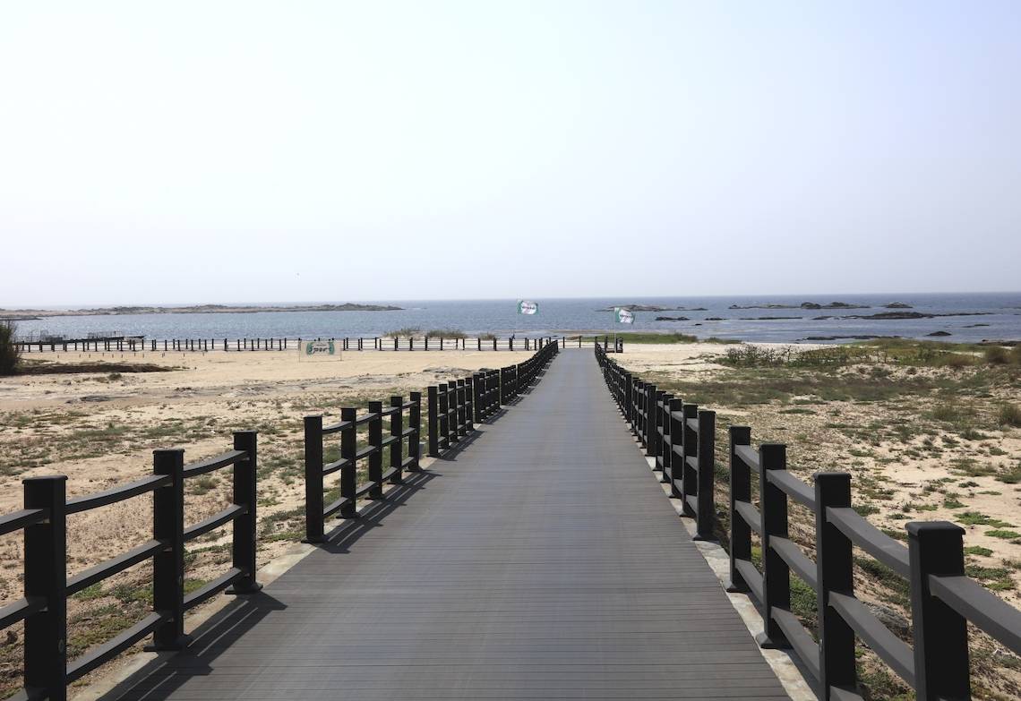 Betonweg zum Strand mit Umzäunung und ruhigen Meeresblick