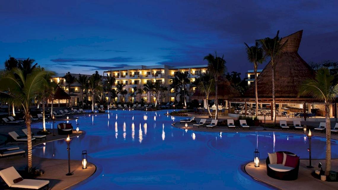 Nachtansicht des Swimmingpools des Secrets Akumal Riviera Maya Hotels, beleuchtet und voll mit Sonnenliegen.