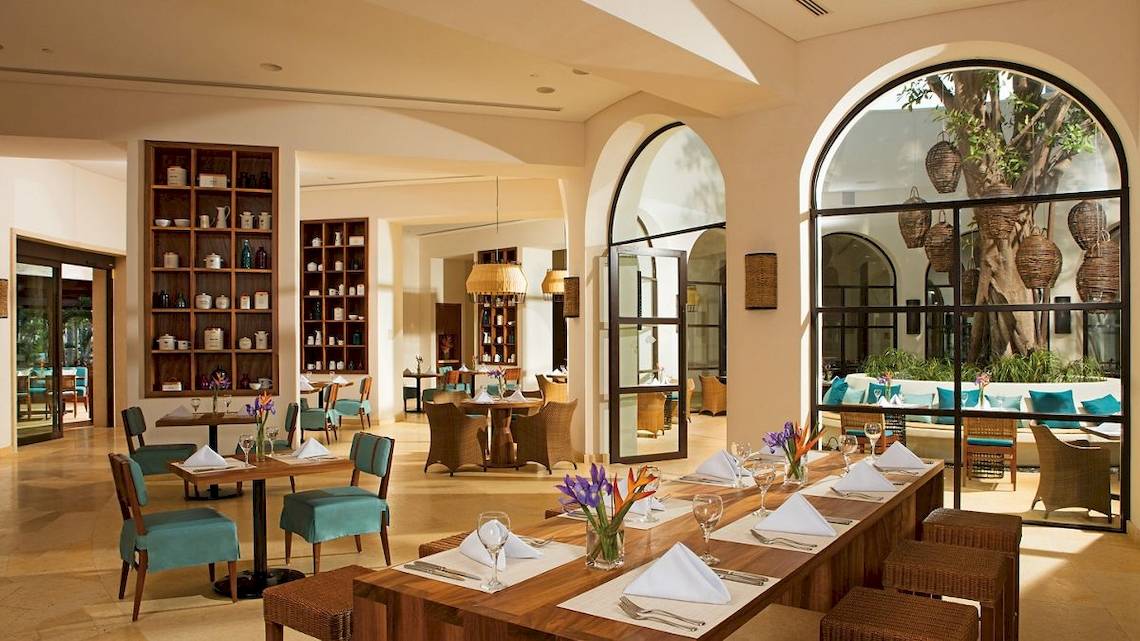 Innenansicht des Restaurants im Secrets Akumal Riviera Maya mit Holztischen, Stühlen und Tischdekoration.