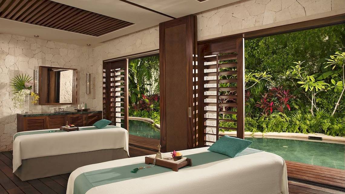 Massageraum im Secrets Akumal Riviera Maya mit Blick auf einen Pool und tropischen Garten.