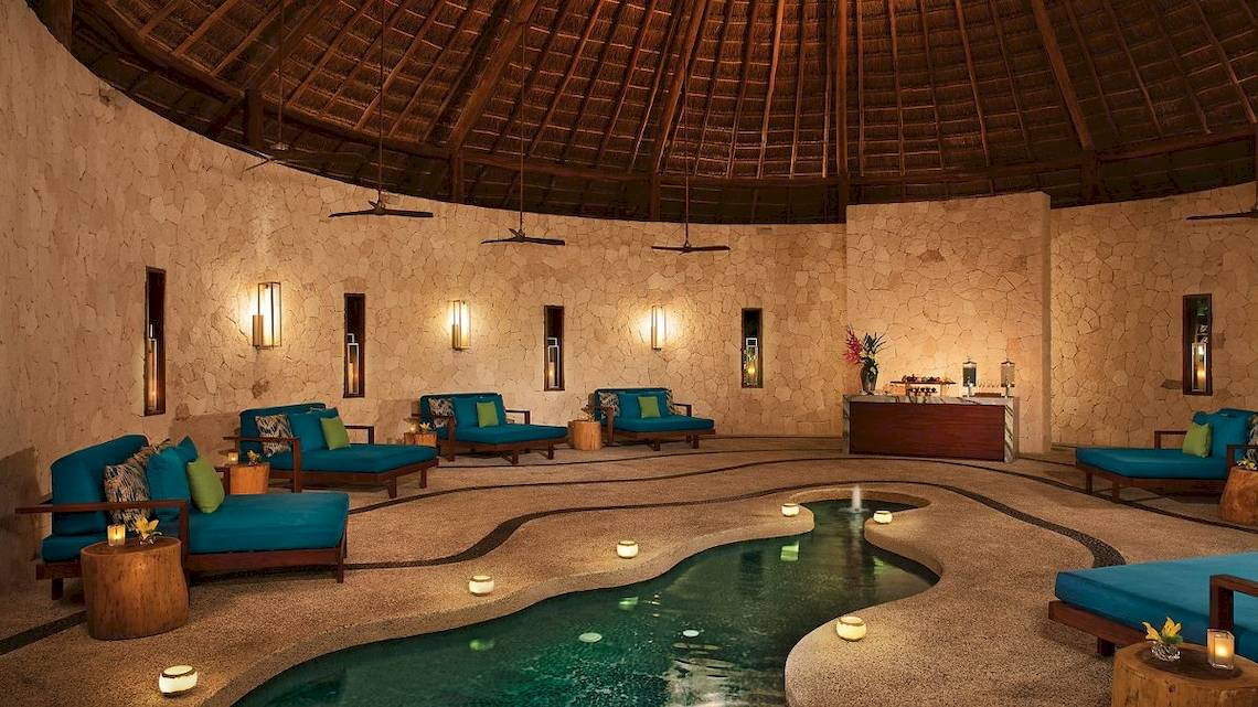 Innenpool des Secrets Akumal Riviera Maya Hotels mit blauen Liegen und Wasserfontäne.