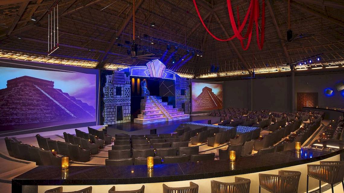 Innenbereich des Theaters im Hotel Secrets Akumal Riviera Maya mit großen Bildschirmen und Sitzplätzen.
