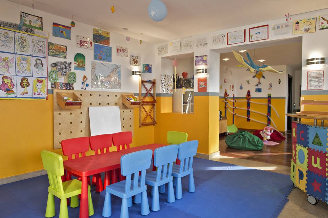 Kinderzimmer im Cove Rotana Resort mit bunten Stühlen, rotem Tisch und dekorierten Wänden.