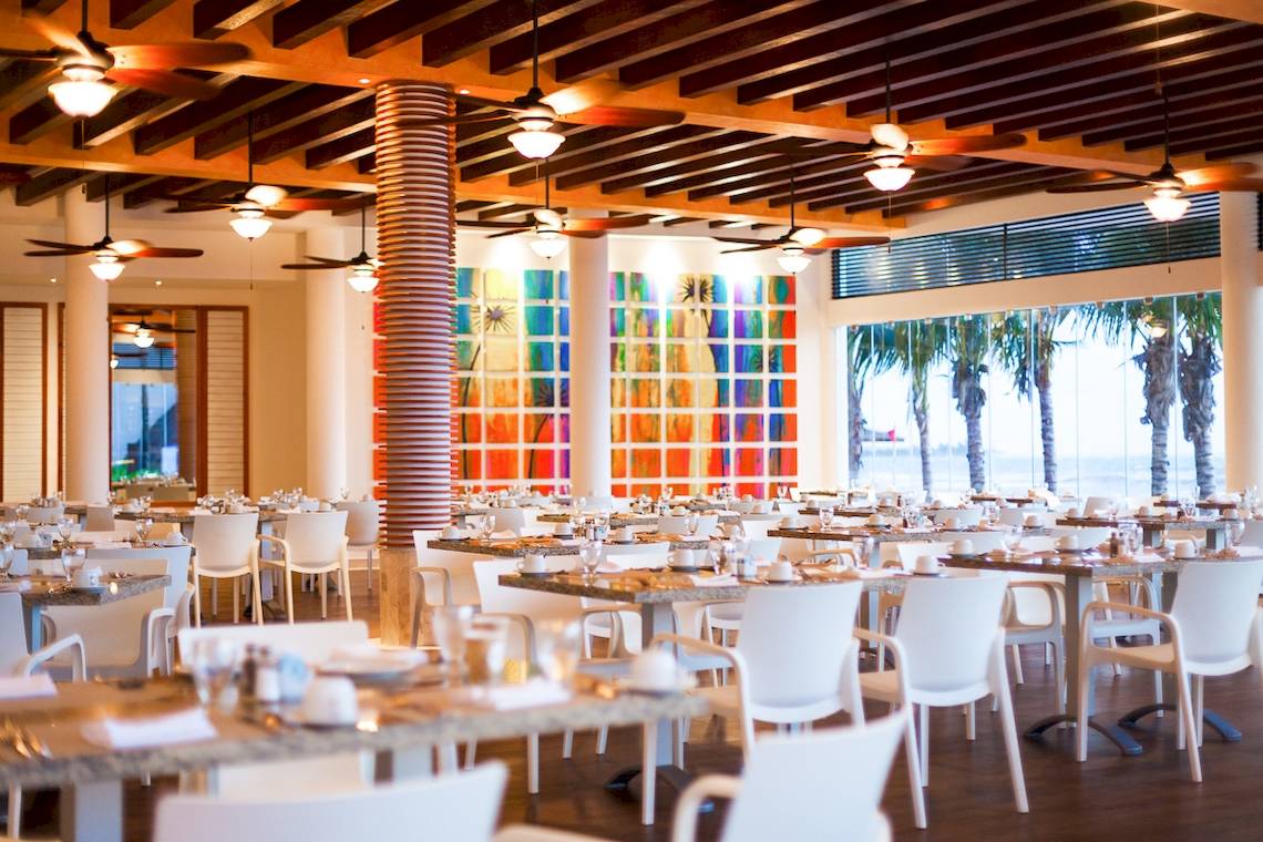 Innenansicht des Restaurants im Reef Coco Beach Hotel mit bunten Wandgemälden und Blick auf das Meer.