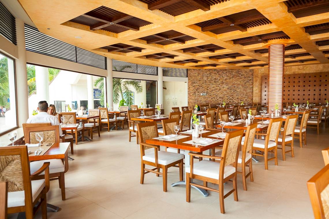 Innenansicht des Restaurants im Reef Coco Beach Hotel mit gedeckten Tischen und Stühlen.