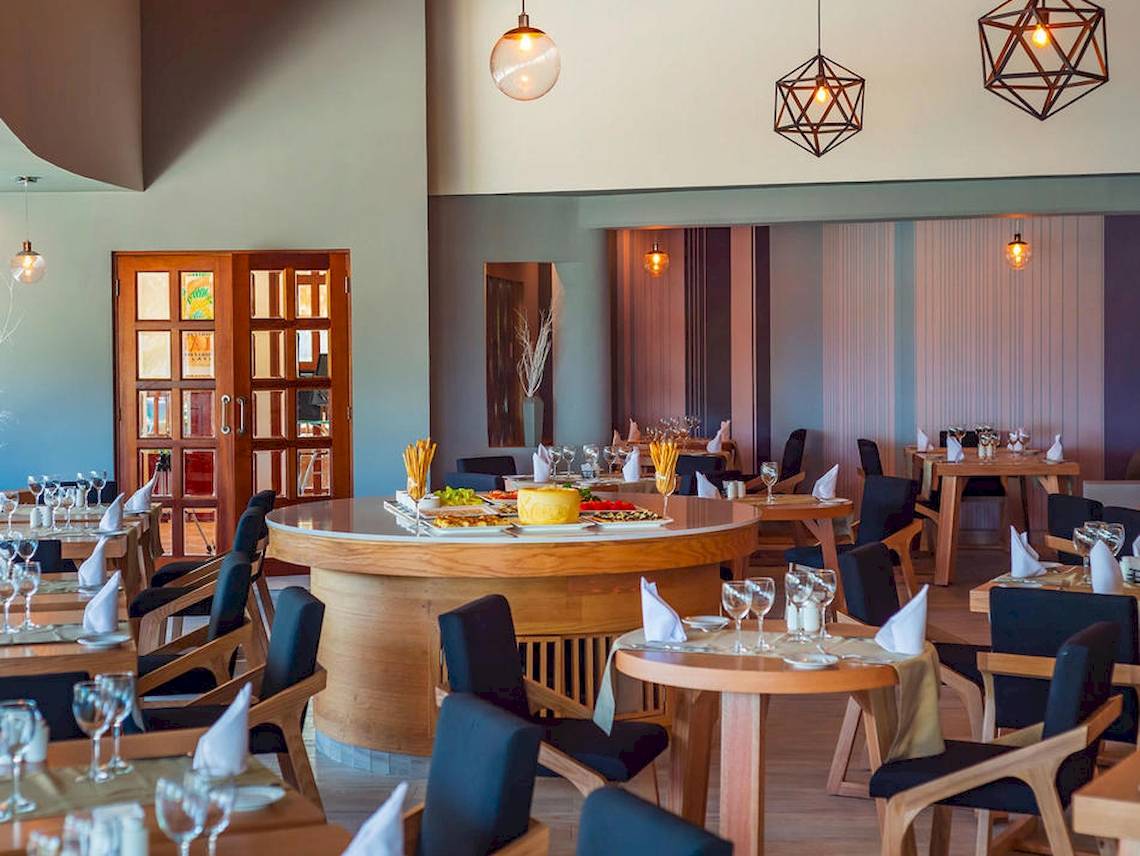 Innenansicht des Restaurants im Reef Coco Beach Hotel mit runden Tischen und Stühlen.