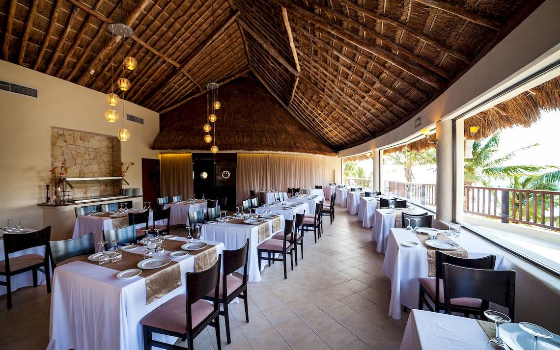 Innenansicht des Restaurants des Reef Coco Beach Hotels mit gedeckten Tischen und hängenden Lampen.