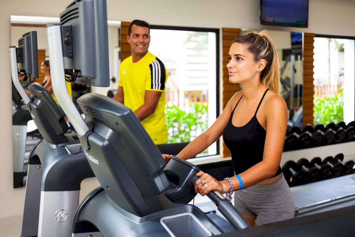 Fitnessstudio im Reef Coco Beach Hotel mit einer Frau auf dem Laufband und einem Mann im Hintergrund.