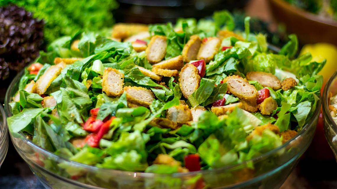 Ein Salat mit grünem Blattwerk, gewürfeltem Huhn und roten Paprikastücken in einer Glasschale.