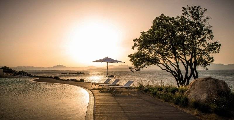 Sonnenuntergang am Cala Cuncheddi Hotel mit Strand, Lounges und einem Schirm