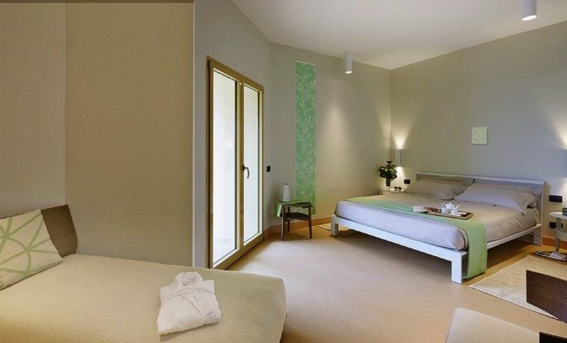 Schlafzimmer im Cala Cuncheddi Hotel mit zwei Betten, einem Nachttisch und einer Glastür.