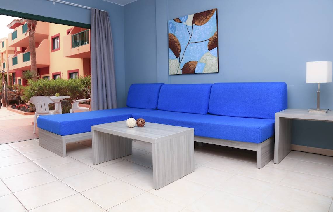 Wohnzimmer im Bluesea Aloe Corralejo Hotel mit blauem Sofa, Tisch und Lampe.