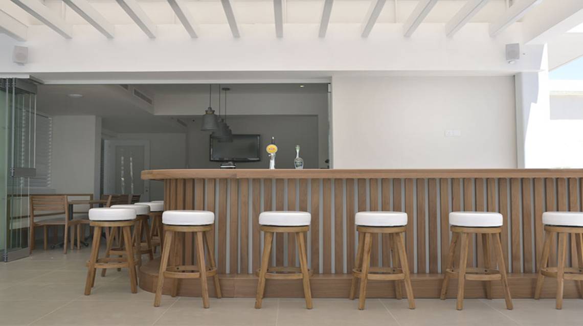 Ein modernes Hotelbar mit Holztheke und weißen Barhockern.