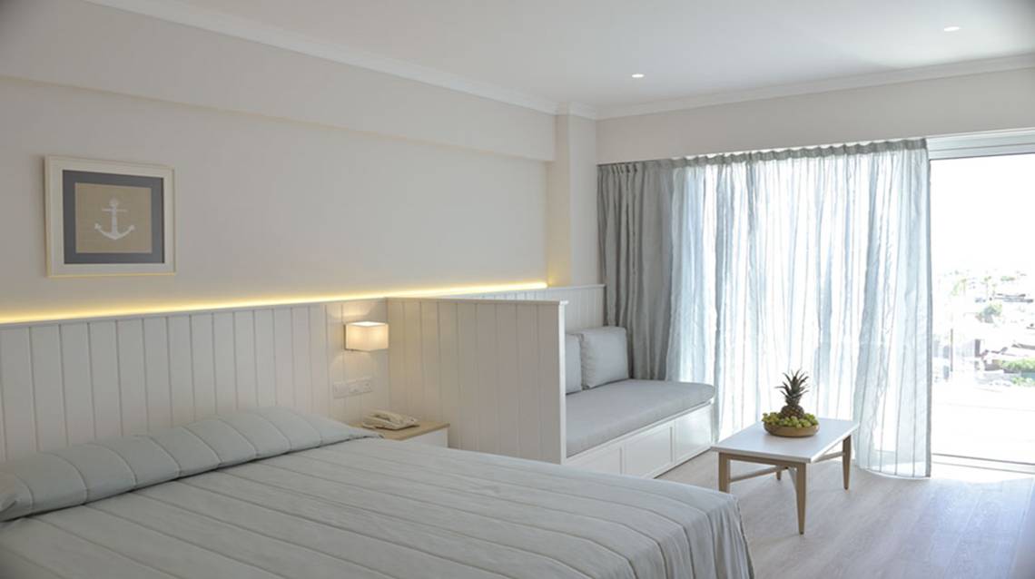 Ein Hotelzimmer im Sunrise Gardens mit weißem Bett, Leseecke und Aussichtsfenster.