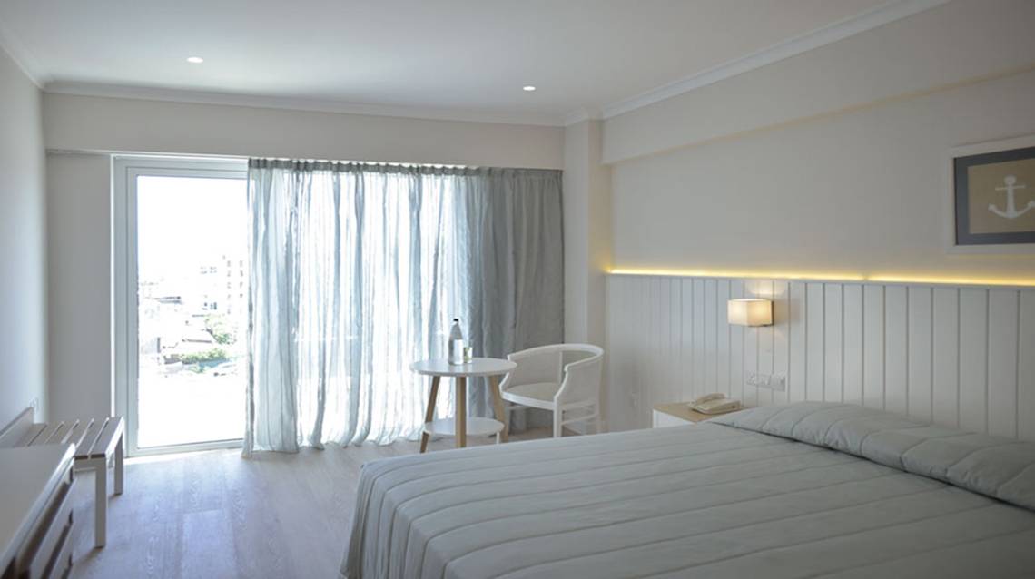 Ein elegantes Hotelzimmer mit Doppelbett, Tisch, Stuhl und einem großen Fenster.