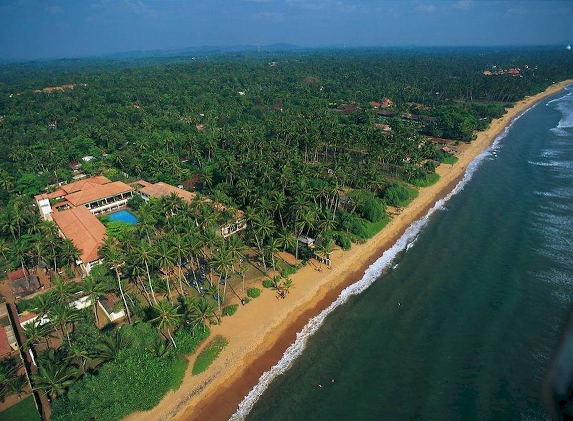 Luftaufnahme des Mermaid Hotel & Club mit Swimmingpool, umgeben von Palmen und einer Küste.
