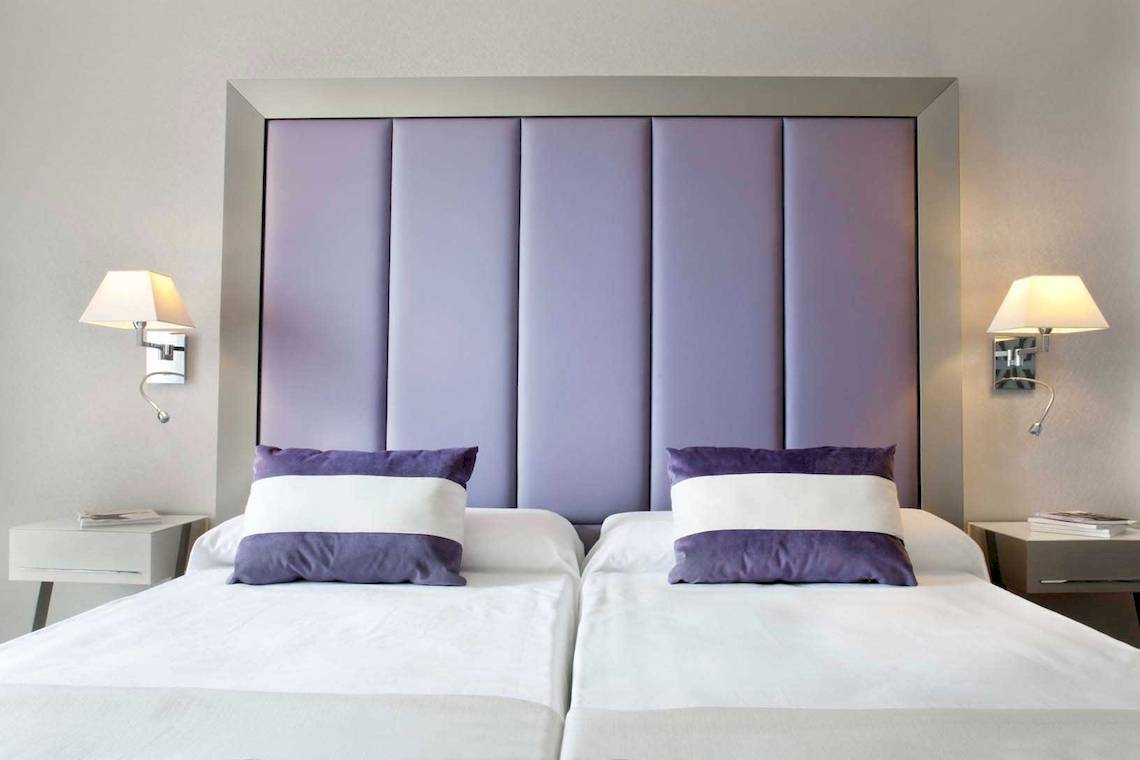 Schlafzimmer mit zwei Betten, lavendelfarbenem Kopfteil und Nachttischen